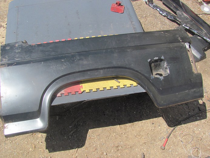 Black rear fender with fuel door opening. Part is on a gray surface