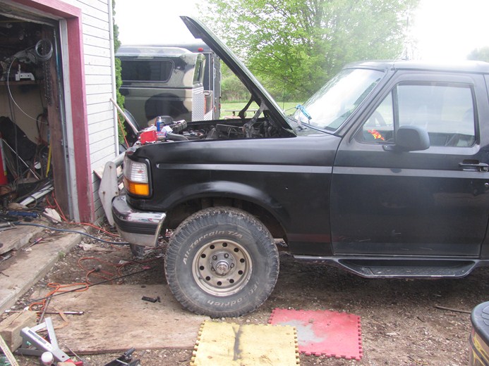 Black 1996 Ford Bronco with hood open, parked in a driveway next to a garage