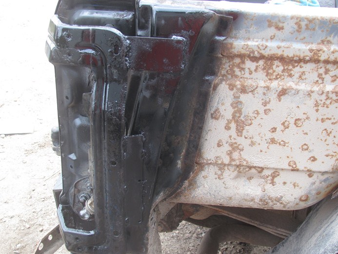 Close-up of a heavily rusted and painted vehicle frame section, showing structural components and corrosion