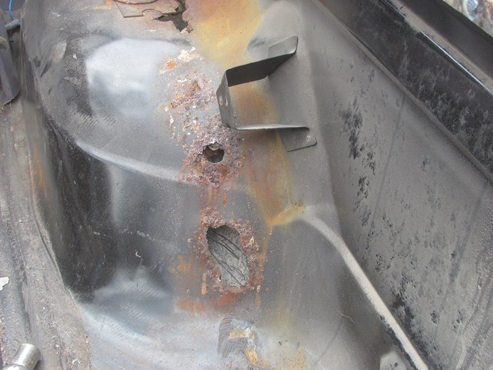 rusted out section of a vehicle's floor pan with a metal bracket attached