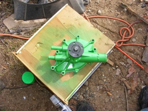 1996 Ford Bronco - A freshly painted green water pump sits on a piece of wood, ready for installation.