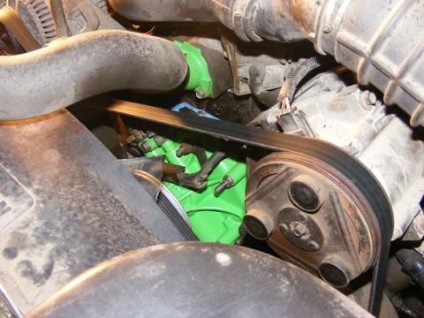 1996 Ford Bronco - Close-up view of engine components, including a green painted part and a serpentine belt system.