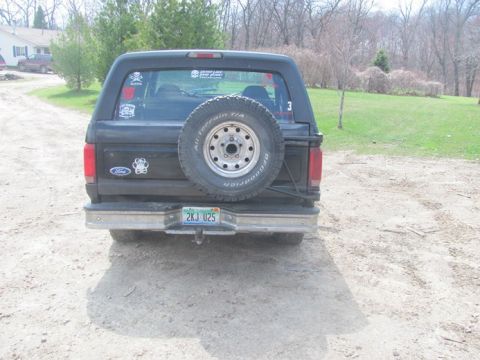 1996 Ford Bronco - Rear view of a black Ford Bronco parked on a dirt road with a spare tire mounted externally.