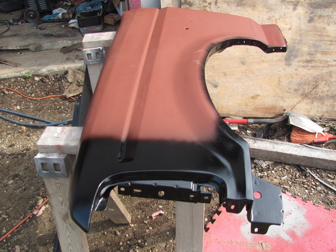 Red and black car fender on sawhorses, showing primer and paint
