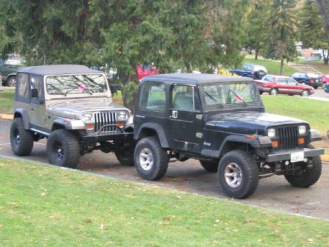 1988 Ford Bronco - A tan Jeep Wrangler is parked next to a black Jeep Wrangler, both facing forward.