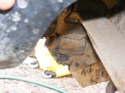 1996 Ford Bronco - A close-up view of a rusty vehicle suspension component, with a yellow jack stand and its wheels in the background.