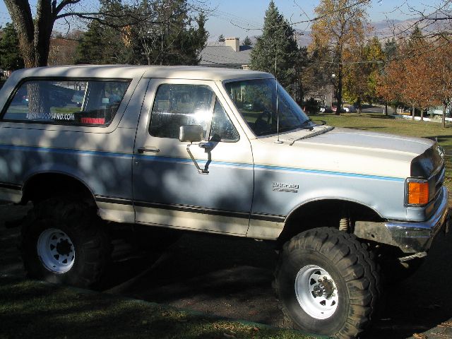 1988 Ford Bronco with large tires, lifted suspension, and blue stripe