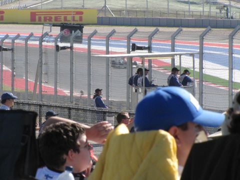 2006 BMW 5 Series - Spectators watch a race from behind fences at a track with a Pirelli banner.