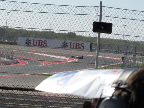 2006 BMW 5 Series - A Formula 1 race car navigates a turn at the Circuit of the Americas, with a prominent UBS advertisement in the background.