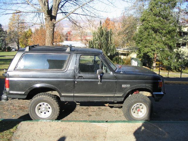 Side view of a dark-colored Ford Bronco with aftermarket wheels and suspension. The word "BRONCO" is visible on the fender