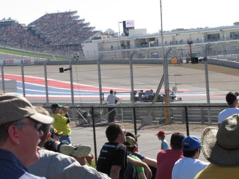 2006 BMW 5 Series - A Formula 1 race car speeds around the track at the Circuit of the Americas, with spectators in the stands.