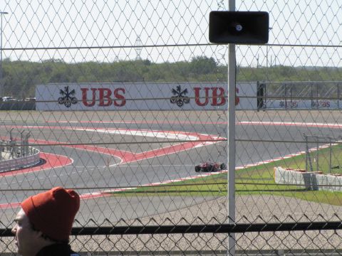 2006 BMW 5 Series - A red race car navigates a turn at the Circuit of the Americas, with a large UBS advertisement visible behind the fence.