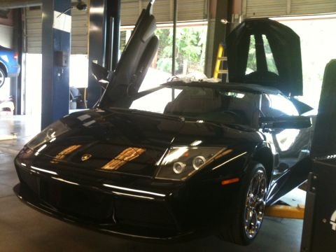 1990 Ford Bronco - A black Lamborghini with its distinctive scissor doors open is parked inside a service bay.