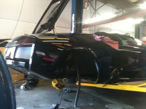 1990 Ford Bronco - Black sports car on a lift in a garage, undergoing maintenance. The front wheel is off.