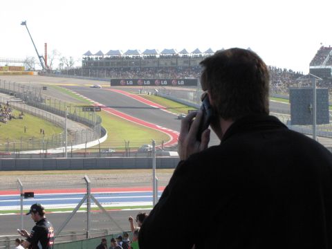 2006 BMW 5 Series - Spectators watch a race from the stands, with a person in the foreground talking on a phone.