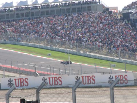 2006 BMW 5 Series - A lone race car navigates the track as spectators fill the grandstands.