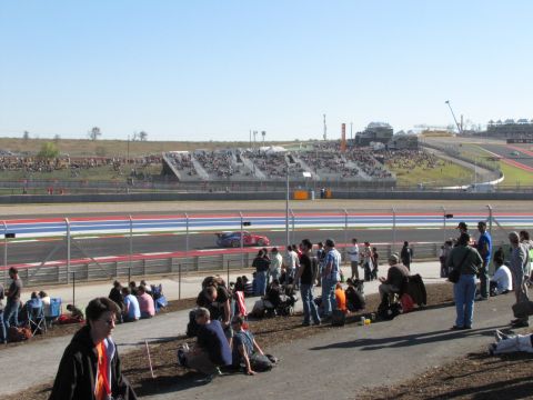 2006 BMW 5 Series - A red race car speeds around a track while spectators watch from the stands and the infield.