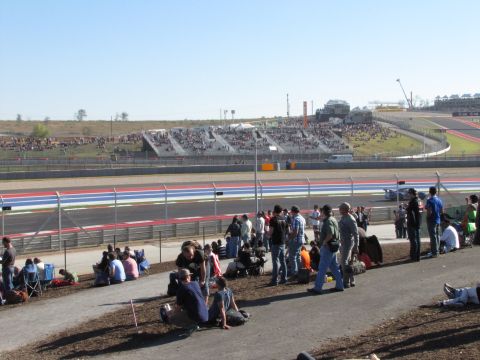 2006 BMW 5 Series - Spectators gather at a race track, with grandstands filled and the track visible in the distance.