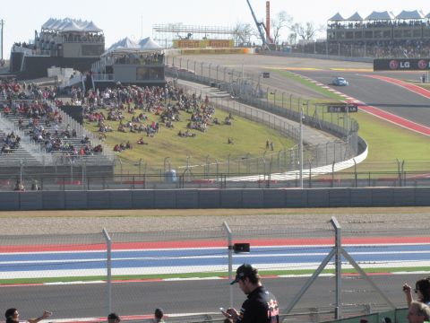 2006 BMW 5 Series - A lone race car navigates the track at the Circuit of the Americas, with crowds gathered in the grandstands.