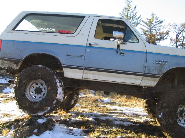 1988 Ford Bronco with large tires on a rocky, snowy trail. "BACKWOODS4WD.COM" sticker on rear window