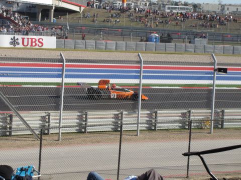 2006 BMW 5 Series - An orange open-wheel race car speeds around a track, with spectators in the stands.