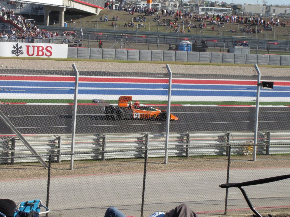 Orange race car with number 9 on it driving on a track. Spectators are in the background