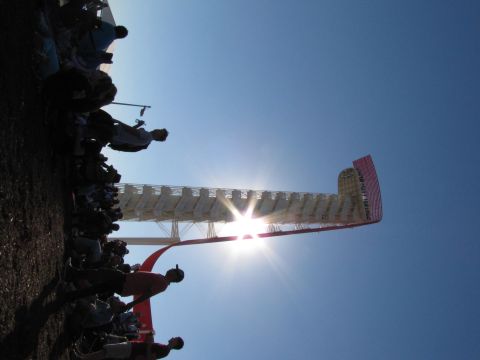 2006 BMW 5 Series - Spectators gather under a bright sun at a race track, with a large, illuminated structure dominating the sky.