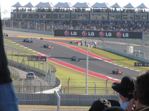 2006 BMW 5 Series - A race is underway with multiple cars on the track and a large crowd watching from the grandstands.