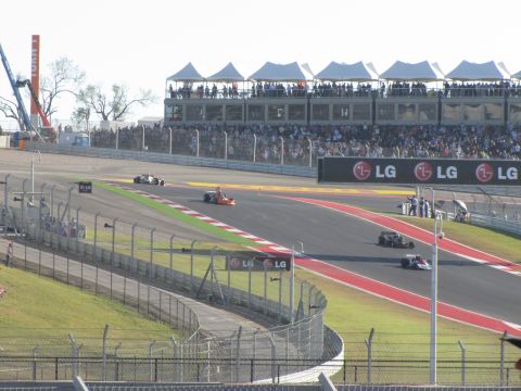 2006 BMW 5 Series - Multiple race cars compete on a track with spectators in the stands and sponsor banners visible.