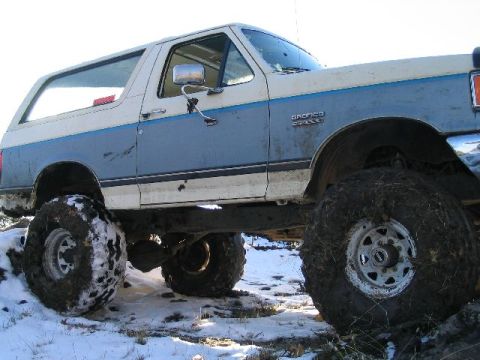 1988 Ford Bronco - This lifted Ford Bronco is shown off-road in a snowy environment, with its large tires covered in mud.