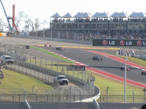 2006 BMW 5 Series - Race cars compete on a track with grandstands full of spectators and sponsor banners.