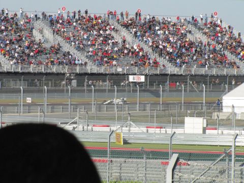2006 BMW 5 Series - A race car speeds around a track with a large crowd watching from the grandstands.