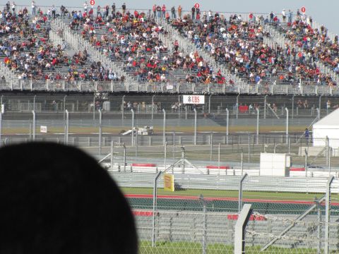 2006 BMW 5 Series - A race car speeds around a track with a large crowd watching from the grandstands.