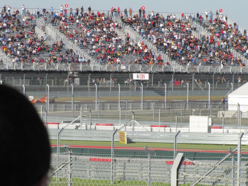 Orange race car on track with spectators in bleachers