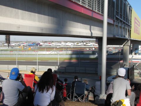 2006 BMW 5 Series - Race cars compete on a track while spectators observe from the stands under an overpass.