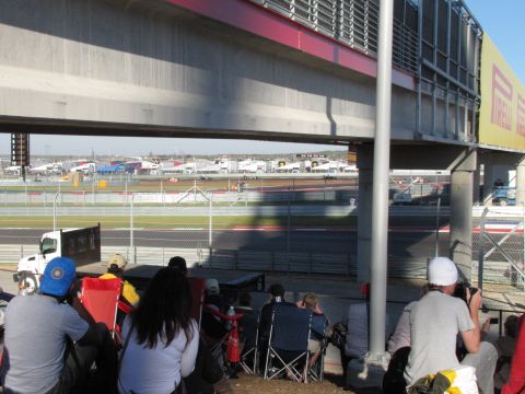 2006 BMW 5 Series - Spectators observe a race event from shaded seating areas beneath a large concrete structure.