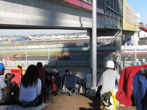 2006 BMW 5 Series - Spectators watch race cars speed around a track from beneath a large concrete structure.