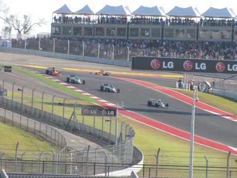 2006 BMW 5 Series - Race cars compete on a circuit with grandstands full of spectators and sponsor signage.
