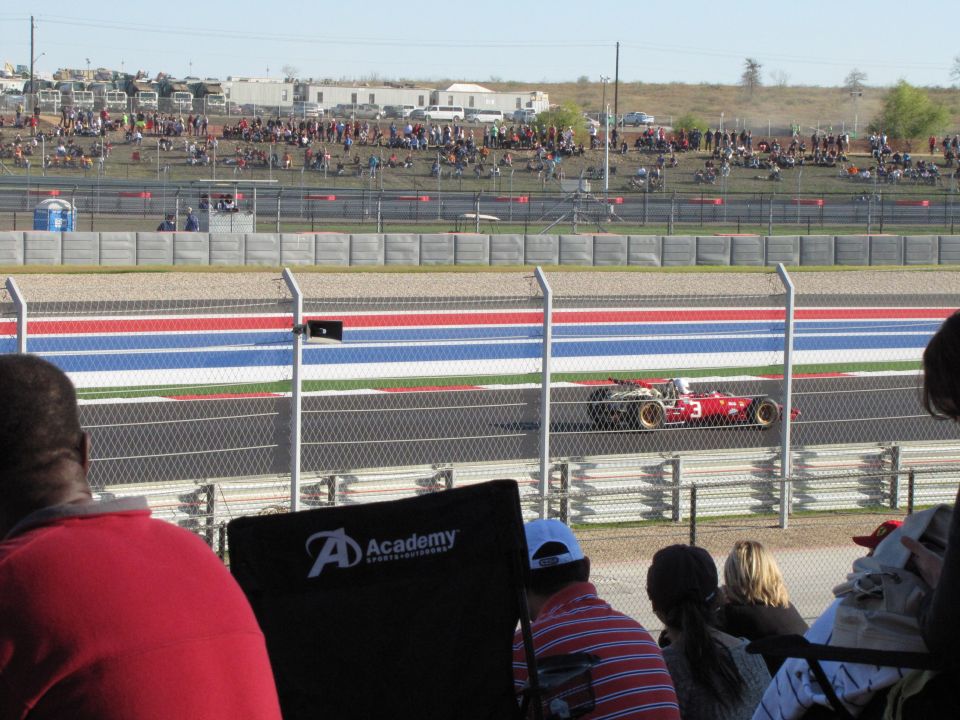 Red Formula 1 race car with gold wheels on a track, spectators in background