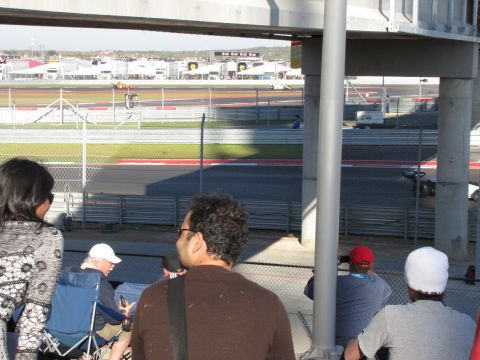 2006 BMW 5 Series - View of a race track and spectators from a grandstand, with distant buildings under a clear sky.