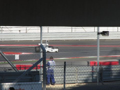 2006 BMW 5 Series - A white race car with the number 8 is seen on a track, with a person in blue overalls standing behind a fence.