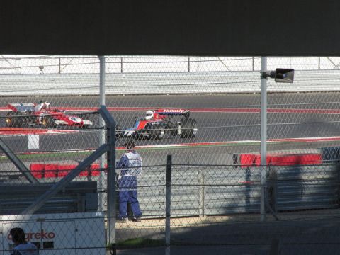2006 BMW 5 Series - Formula 1 cars compete on a race track, with a crew member in blue standing trackside.