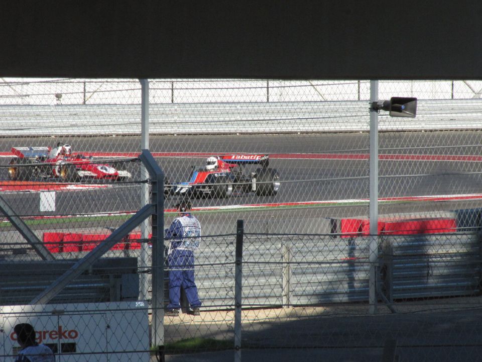 Two Formula 1 race cars on a track, one in red and white, the other in blue and red with 'Tabatic' visible