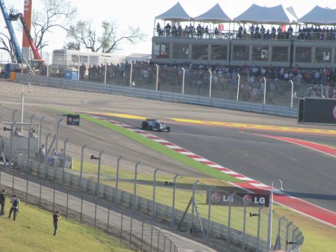 2006 BMW 5 Series - A Formula 1 race car speeds around a track with grandstands full of spectators.