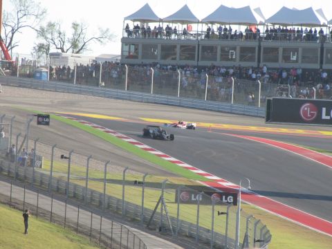 2006 BMW 5 Series - Race cars compete on a track with grandstands full of spectators and sponsor signage.