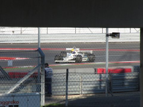 2006 BMW 5 Series - A Formula 1 race car competes on a track, viewed through a fence.