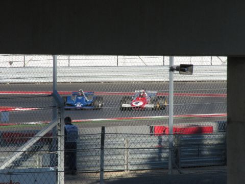 2006 BMW 5 Series - Two race cars compete on a circuit, viewed through a fence.
