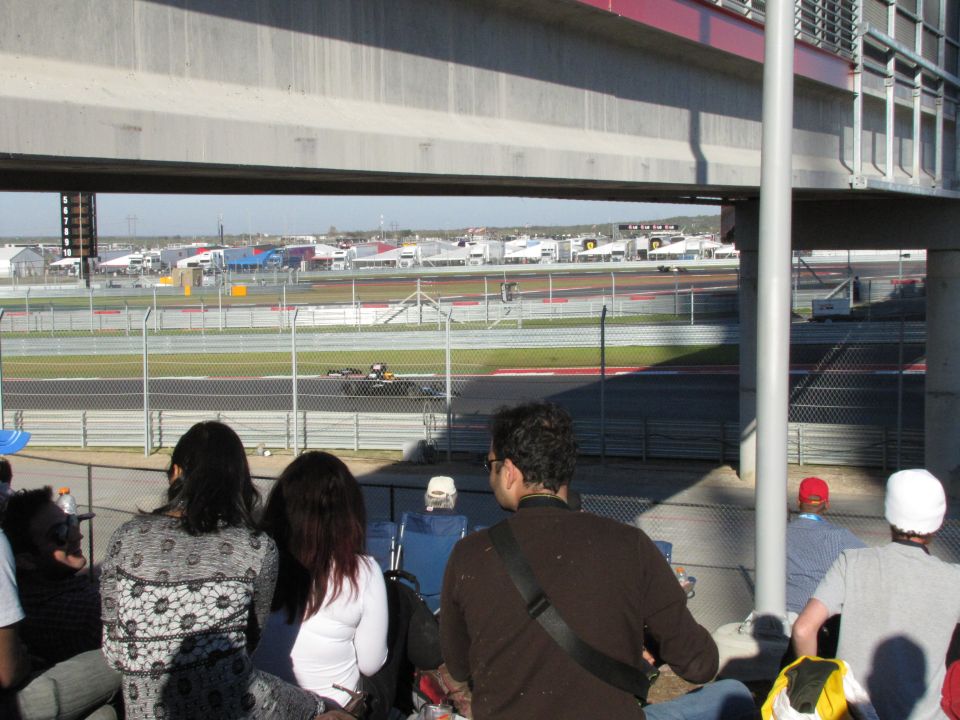 Race car on track with spectators in foreground under bridge