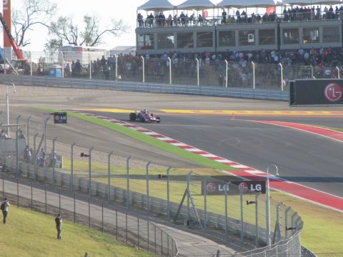 2006 BMW 5 Series - A race car navigates a turn at a circuit with grandstands and sponsor logos visible.