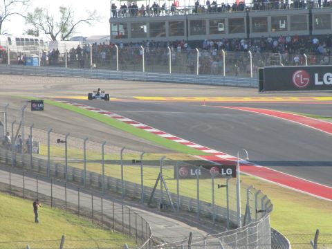 2006 BMW 5 Series - A lone race car navigates a turn at a circuit with spectators watching from above.